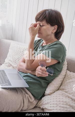 Caucasian mature woman suffers eye strain when using a laptop at home Stock Photo