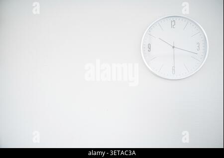 White round clock on a white wall. the clock is located in the upper right part. space for an inscription. the clock shows 10.18 Stock Photo
