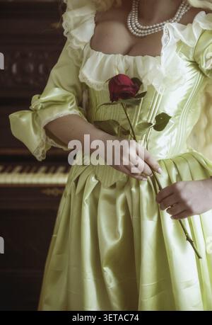 Close-up of a medieval dress corset and corset. pearls on the neck. soft green rococo style dress. red rose in hands. photo without a face. black pian Stock Photo