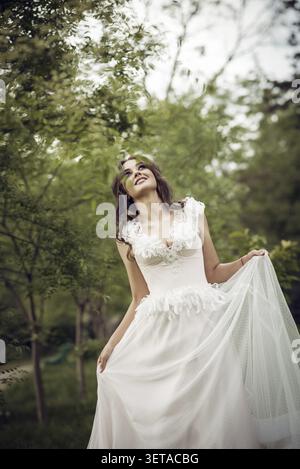 Stunning Bride Gracefully Poses in Spring Park Among Blossoming Trees. Exuding Elegance, Romance and Timeless Charm. Soft Pink Wedding Dress with Euro Stock Photo