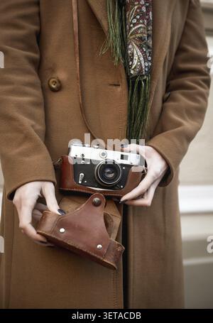 Front view of a vintage camera. In a woman's hands is an SLR camera with film from the 1970s. The camera has a brown leather case. A Woman in a Brown Stock Photo