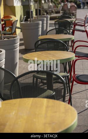 Street Cafe Tables with Bright Red Chairs and Green Furniture, with Plants in Large Pots Wooden table surface, close-up, foreground. Empty cafe on the Stock Photo