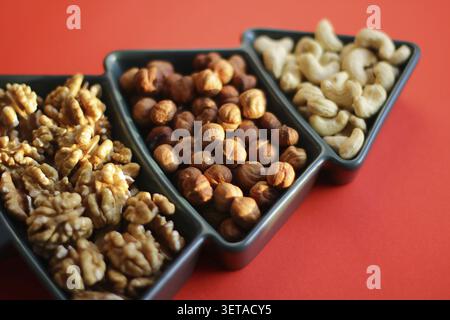 Different types of nuts Different snacks for the New Year's table in a plate in the shape of a Christmas tree. cashew nuts, hazelnuts, almonds Stock Photo