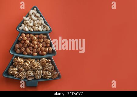 Different types of nuts Different snacks for the New Year's table in a plate in the shape of a Christmas tree. cashew nuts, hazelnuts, almonds Stock Photo
