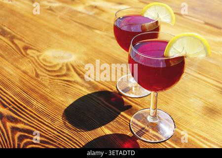 Two glasses of red summer cocktails with lemon slices on a wooden background Stock Photo