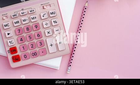 Work table with top view. On a pink background, a pink calculator, a blank notepad for notes, a pencil Stock Photo