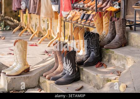 A collection of handcrafted cowboy boots displayed on stone steps outside a leather goods shop in Hanoi, Vietnam. Stock Photo