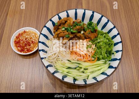 Bun Thit Nuong is a popular Vietnamese noodle dish featuring grilled marinated pork served over rice vermicelli, topped with fresh vegetables and herb Stock Photo