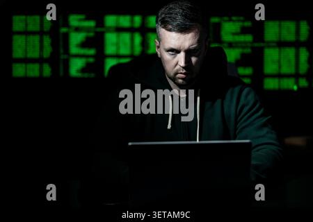 Hacker uses laptop for hacking activity. Hacker analyzes encryption and firewall system. Hacker monitors digital data flow. Hacker attempts identity Stock Photo