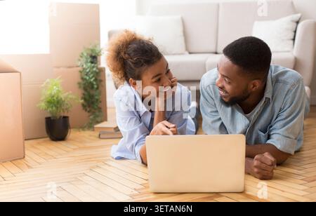 Spouses Using Laptop Lying On Floor Among Moving Boxes Indoor Stock Photo