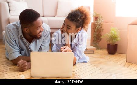 Afro Couple Using Laptop Lying On Floor In New House Stock Photo