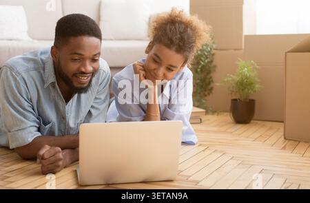 Joyful Spouses Using Laptop Lying On Floor In New House Stock Photo