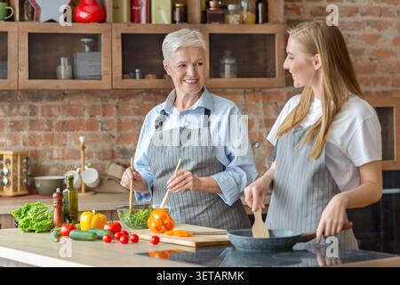 Two Women Preparing a Fresh Salad Together in a Cozy Kitchen During Daytime Cooking Session Stock Photo