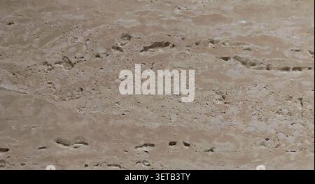 A close-up of natural travertine stone showing irregular cavities, horizontal veining, and a pitted surface in warm cream and beige tones. Stock Photo