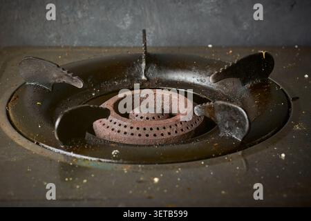 old rusted gas stove burner head with dirty black metal pan supports and food crumbs, greasy unhygienic kitchen appliance in closeup view Stock Photo