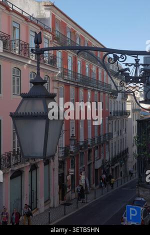 Ornate Black Wrought Iron Street Lamp Bracket Close-Up with Pink Terracotta Buildings and Steep Street Scene in Lisbon Chiado Stock Photo