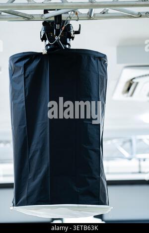 Close-up of large cylindrical softbox suspended from truss, with black exterior and white diffusion panel, symbolizing professional studio and video p Stock Photo