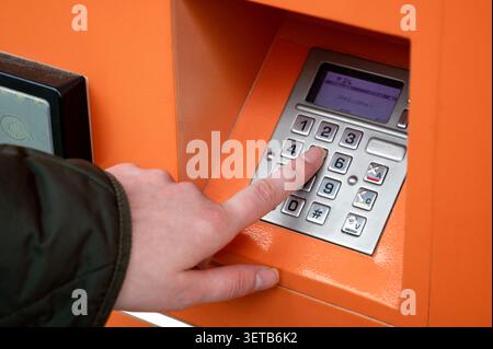 Close up of hand entering PIN code on parcel locker keyboard. Automated orange post terminal interface. Receiving and sending package Stock Photo