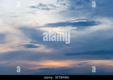 Soft blue evening sky layered with wispy and billowing clouds, lit by a warm sunset glow near the horizon. Calm, atmospheric scene that conveys sereni Stock Photo