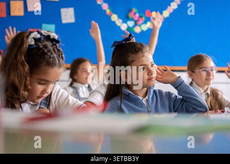 Group of elementary school students actively participating in a classroom lesson by raising their hands to answer questions. Stock Photo