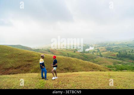 Two young men converse on a hilltop with a scenic, misty landscape stretching out below in Banswara, Udaipur, Rajasthan. Stock Photo