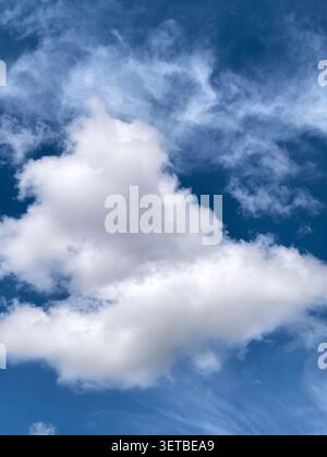 Large bright cloud illuminated by daylight against a rich blue sky with wispy cirrus formations. Natural atmospheric background. Stock Photo