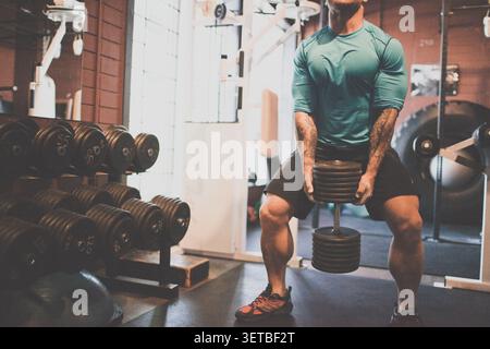 Muscular man with tattoos lifting heavy dumbbell Stock Photo