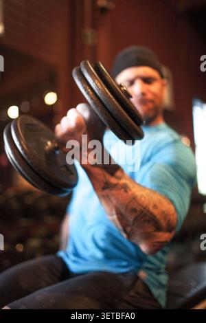 Muscular man with tattoos doing bicep curls Stock Photo