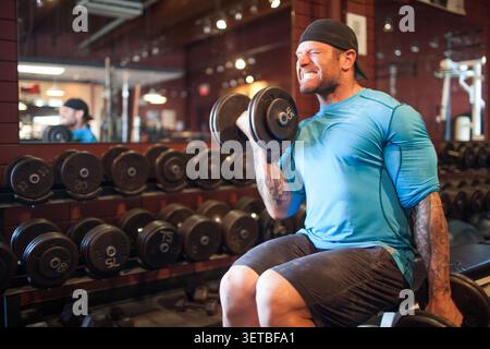 Muscular man with tattoos doing bicep curls Stock Photo