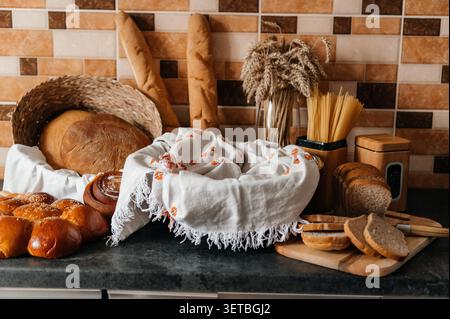 A charming and warm wide-angle shot of a kitchen counter filled with a variety of freshly baked goods, including round loaves in a wicker basket, Stock Photo