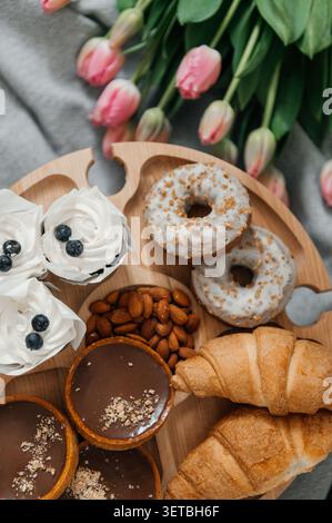 A beautiful high-angle shot of a wooden serving tray filled with delicious treats, including glazed donuts, chocolate tarts, fresh croissants, Stock Photo