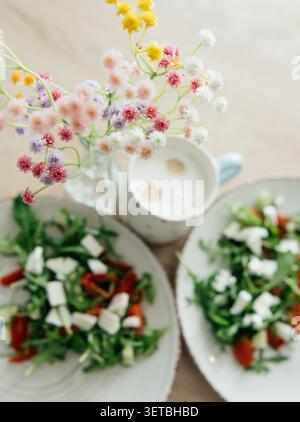 A top-down view of a cozy morning breakfast featuring two plates of fresh vegetable salad with arugula, cherry tomatoes, cucumbers, and feta cheese. Stock Photo
