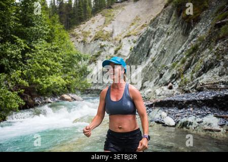 Smiling woman trail running through a mountain creek Stock Photo