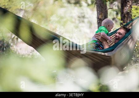 Happy father and baby relaxing in a forest hammock Stock Photo