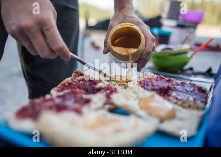 Man pouring peanut butter onto bread for sandwiches Stock Photo