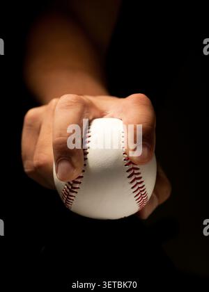 Close up of a hand gripping a baseball against a black background Stock Photo