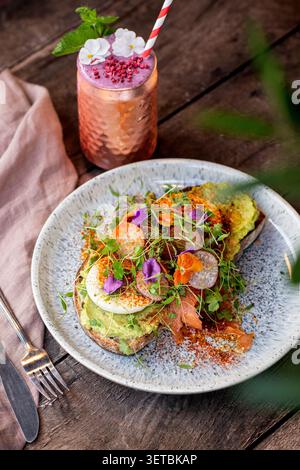 Artisanal sourdough avocado toast topped with a soft-boiled egg, smoked salmon, radish, fresh microgreens, and edible flowers. Stock Photo