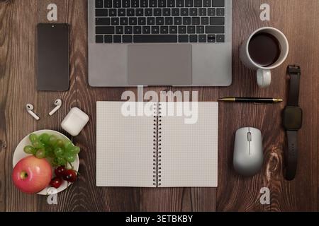 Flat lay of laptop notebook and healthy fruit snack on wooden desk for remote work productivity Stock Photo