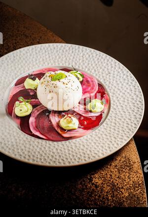 Fresh burrata cheese served over thin slices of beetroot carpaccio, garnished with cream dollops and microgreens. Stock Photo