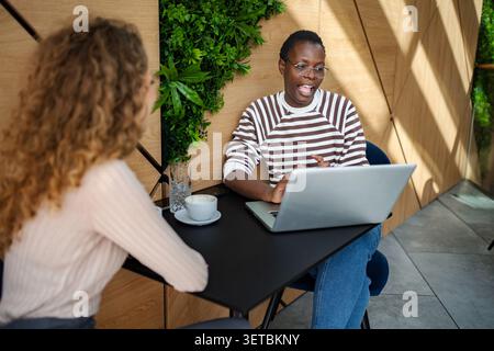 Diverse women collaborating on laptop and communicating ideas in cafe Stock Photo