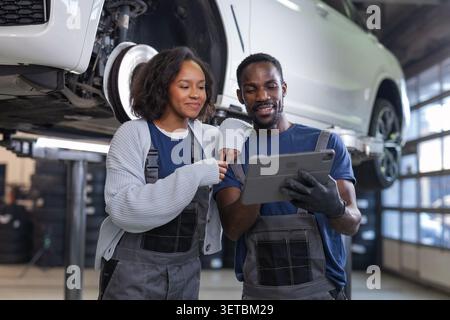 Two auto mechanics check vehicle data on a digital tablet in an automotive workshop. They work on vehicle maintenance together. Stock Photo