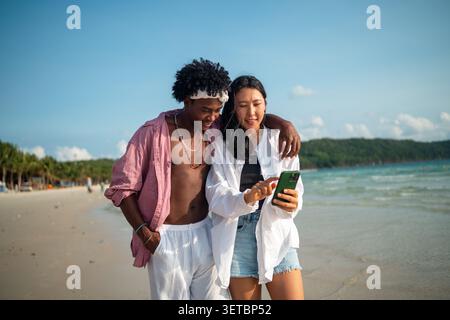 Trendy digital creator couple taking selfie by the beach, sharing travel content for social media Stock Photo