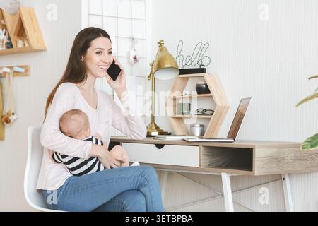 Young Mother Working From Home While Holding Baby and Talking on Phone Stock Photo