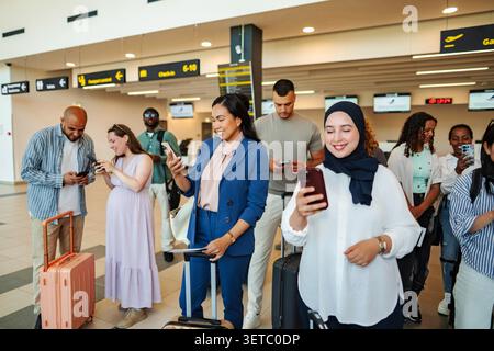 Diverse adults using mobile devices while waiting in a busy airport terminal Stock Photo