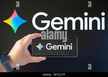 ZHONGSHAN China-June 19 2026: hand holding a smartphone displays the colorful Gemini AI logo against a monitor with the same logo. Stock Photo