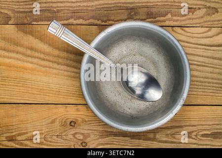 Aluminum bowl with a spoon on the background of wood. An old aluminum plate on wooden boards. Stock Photo