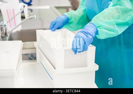 The technician wears protective medical clothing while preparing sterile equipment boxes in a clinical workspace, demonstrating high hygiene standards Stock Photo