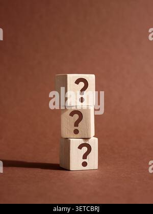Stack of three wooden cubes with question marks on brown background representing frequently asked questions, problem solving and business solution Stock Photo