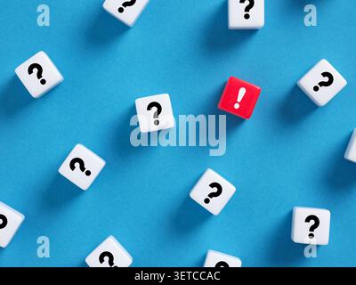 Red exclamation mark cube standing out among white question mark cubes, symbolizing finding a solution or answer to a problem Stock Photo