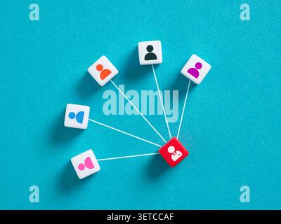 Red cube representing a leader connecting with team members, forming a centralized network structure on a blue background Stock Photo